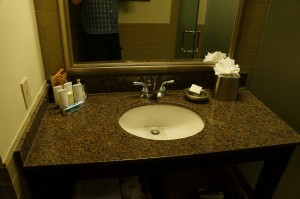 a sink with a mirror and a person standing in the background