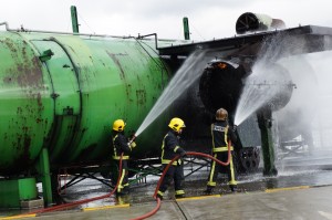 firefighters spraying water on a large green tank